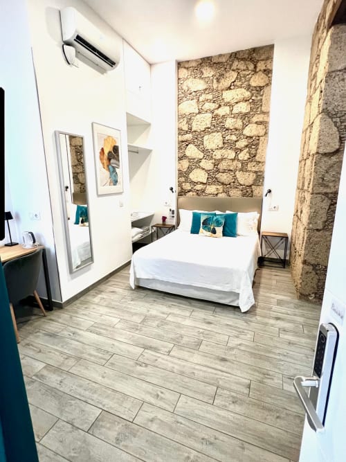Habitación doble moderna en Hotel The Cathedral Vegueta con paredes de piedra, ropa de cama blanca, aire acondicionado y suelo de madera