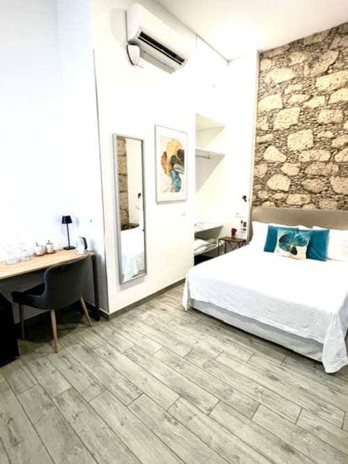 Modern double room at Hotel The Cathedral Vegueta with stone accent wall, white bed, desk, and AC unit in Las Palmas