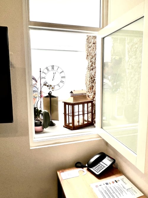 Hotel room window nook with desk, phone, clock, potted plant, and wooden display cabinet at Hotel The Cathedral Vegueta