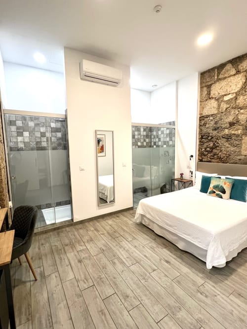 Habitación Deluxe moderna en Hotel The Cathedral Vegueta con cama queen, ducha cristal, piso de madera y pared de piedra vista
