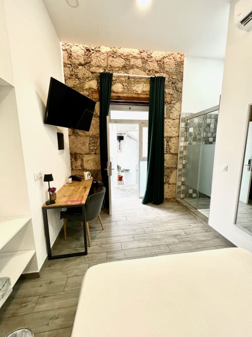 Habitación moderna del hotel The Cathedral Vegueta con pared de piedra, escritorio, TV y entrada de baño acristalada en Las Palmas