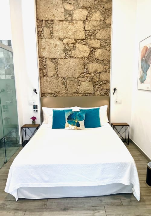 Habitación moderna en Hotel The Cathedral Vegueta con cama blanca, almohadas turquesas y pared de piedra vista en Las Palmas