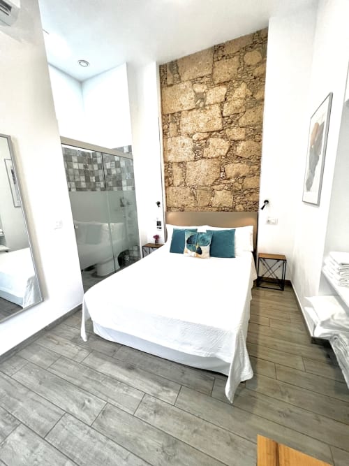 Moderno dormitorio doble en Hotel The Cathedral Vegueta con pared de piedra vista, ropa de cama blanca y suelo de madera