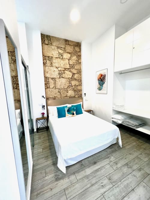 Moderno dormitorio doble en Hotel The Cathedral Vegueta con pared de piedra, ropa blanca, almohadas turquesas, decoración de madera
