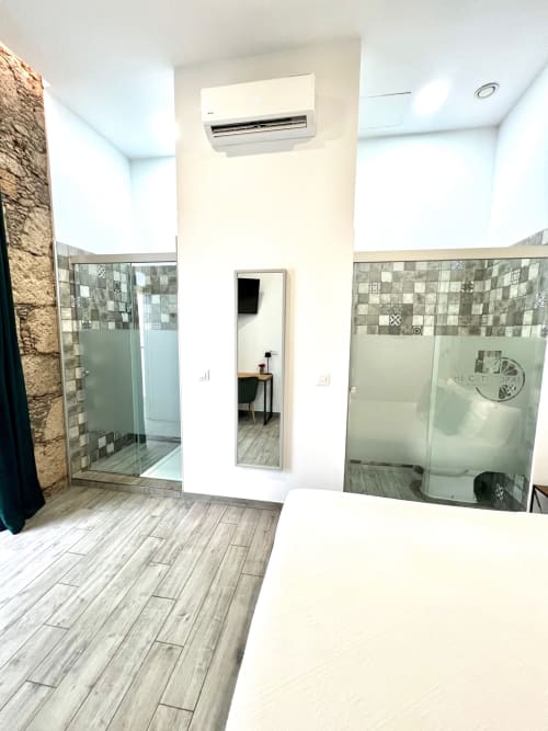Baño moderno con dos cabinas de ducha, pisos con acabado gris tipo madera y aire acondicionado mural en Hotel The Cathedral