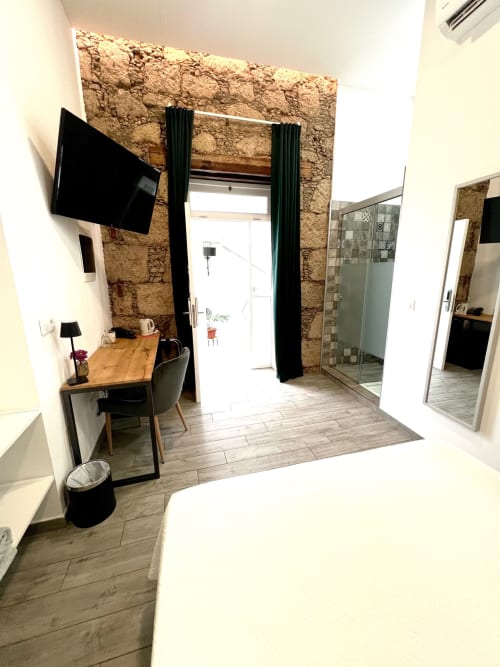 Habitación doble moderna en Hotel The Cathedral Vegueta con pared de piedra, TV, escritorio y baño en suite en Las Palmas
