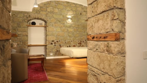 Sypialnia ze ścianami z kamienia w Sardegna Explora House z drewnianymi podłogami, łóżkiem, czerwonym dywanem i rustykalnym wystrojem w Magomadas, Włochy