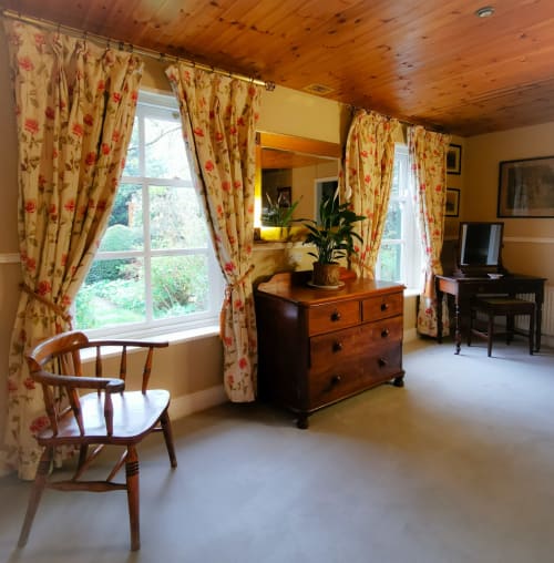 Bright bedroom in The Garden House cottage at Kilmokea Manor with floral curtains, wooden dresser, mirror, and garden views