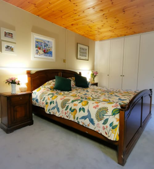 Spacious bedroom in The Garden House cottage at Kilmokea Manor with wooden ceiling, floral bedding, dark wood bed frame, and