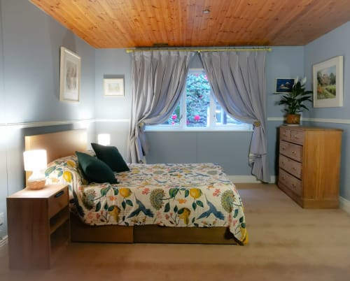 Bright bedroom in The Garden House cottage at Kilmokea Manor, featuring floral bedding, wooden ceiling, grey curtains, and