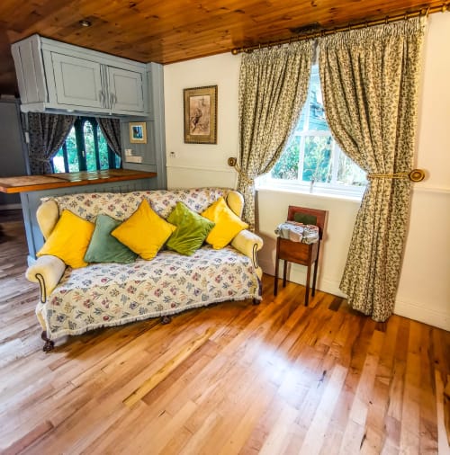 Cozy cottage sitting room at Kilmokea Manor with floral sofa, yellow cushions, window views, and wooden beams