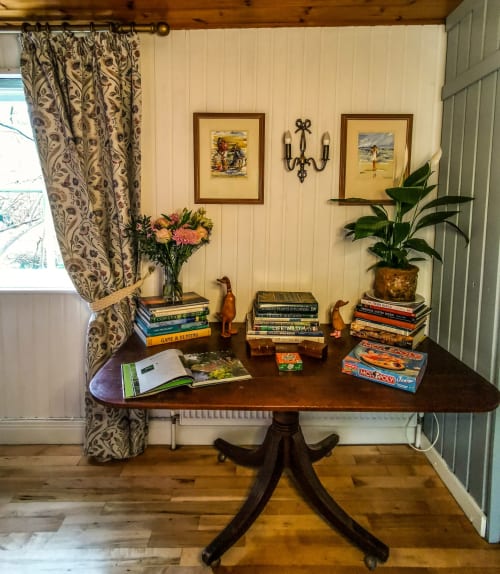 Elegant cottage room at Kilmokea Manor with dark wood pedestal table, stacked books, potted plant, decorative framed prints,
