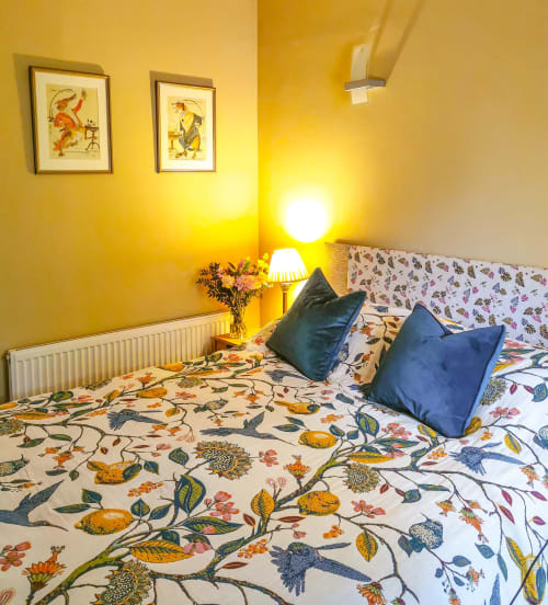 Bright yellow bedroom at Kilmokea Country Manor with floral bedding, blue pillows, and framed artwork in The Garden House