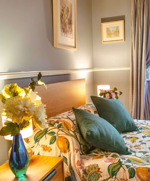 Bright bedroom at Kilmokea Manor with floral bedding, green pillows, yellow flowers in blue vase, and framed botanical art on