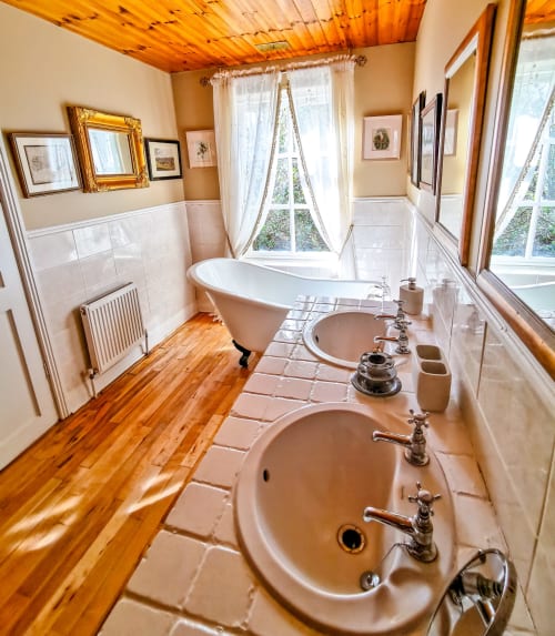 Elegant bathroom at Kilmokea Country Manor with dual sinks, freestanding bathtub, wooden ceiling, and garden views in