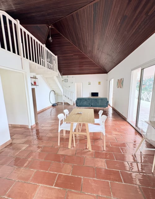 Spacieux séjour avec table à manger, chaises blanches, plafond en bois et carrelage terre cuite à La Conciergerie