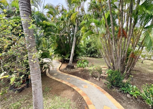 Allée courbe en briques à travers un luxuriant jardin tropical avec palmiers à la villa La Conciergerie Martinique aux Trois-Îlets
