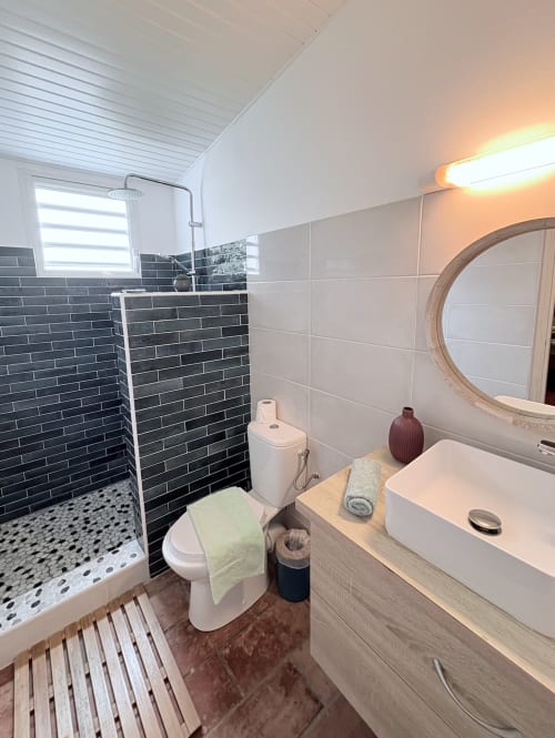 Salle de bain moderne à La Villa Adele en Martinique avec douche aux carreaux sombres, vasque blanche et miroir rond