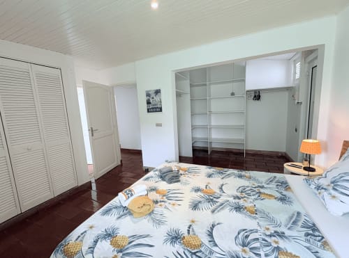 Chambre spacieuse à La Villa Adele en Martinique avec literie ananas tropical, placards à persiennes et plafond blanc lumineux.