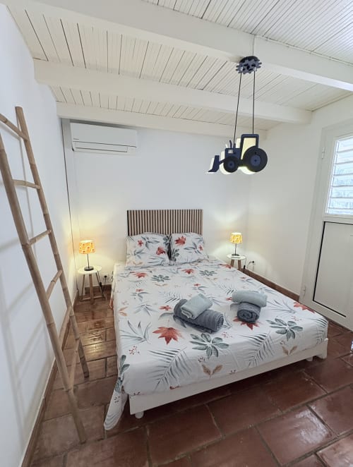 Chambre lumineuse à La Conciergerie Martinique avec literie fleurie, suspension rétro et carrelage terre cuite