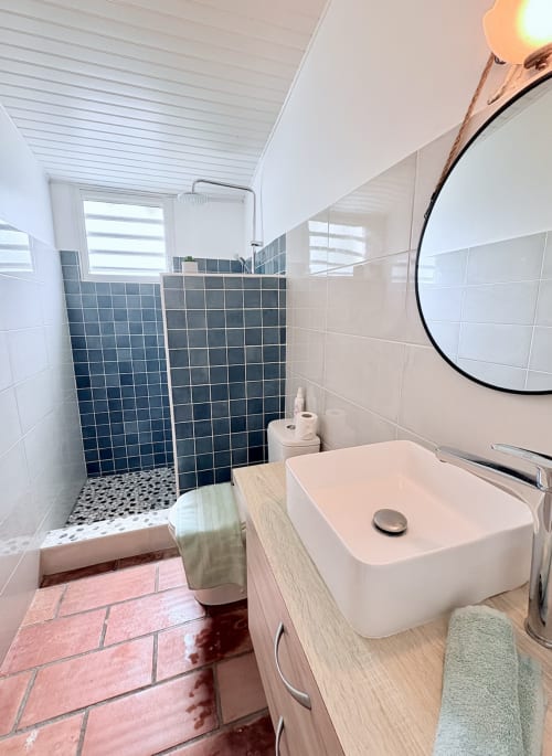 Salle de bain moderne avec douche à l'italienne, lavabo blanc et carrelage à la villa La Conciergerie Martinique