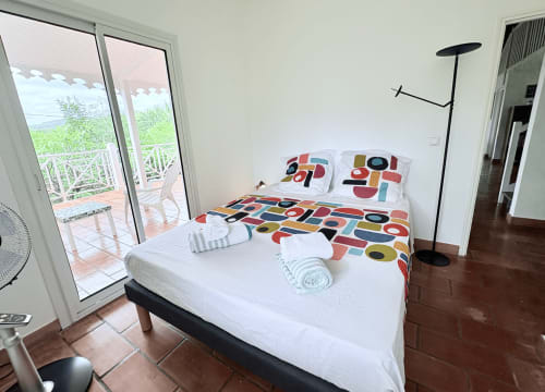 Chambre lumineuse de la villa La Conciergerie Martinique avec literie colorée, accès terrasse et vue sur la piscine aux Trois-Îlets