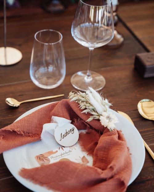 Un élégant couvert à La Villa Tosca B&B à Callas avec serviette terracotta, assiette blanche et verres à vin sur table en bois.