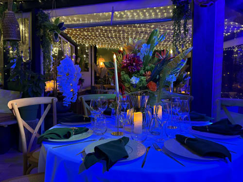 Élégante table dressée en terrasse à La Villa Tosca B&B à Callas, avec éclairage ambiant bleu, chaises blanches et compositions florales colorées