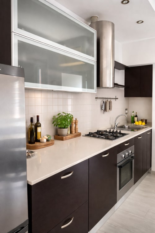 Modern kitchen with dark cabinets, white countertop, gas stove, and glass upper cabinets at Hbhall Navigli 15 apartment in