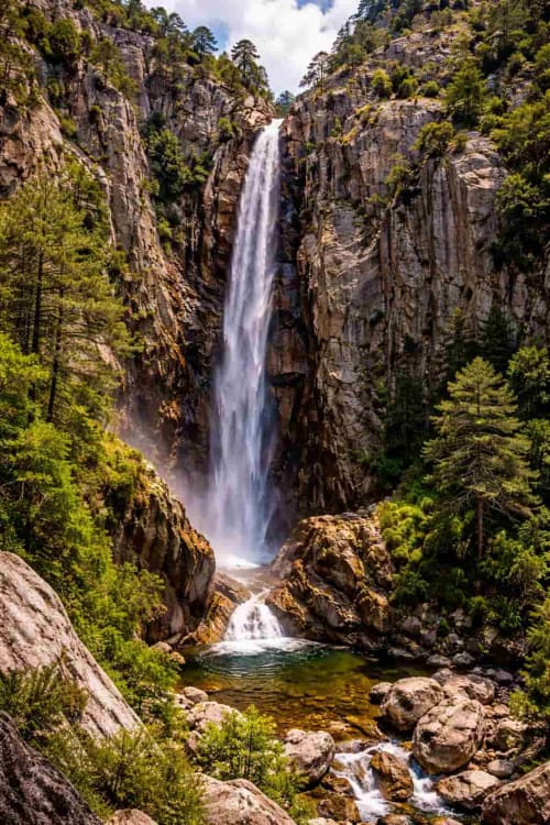 Spectaculaire cascade dégringolant dans un canyon rocheux bordé de forêts de pins, près de Porto-Vecchio en Corse