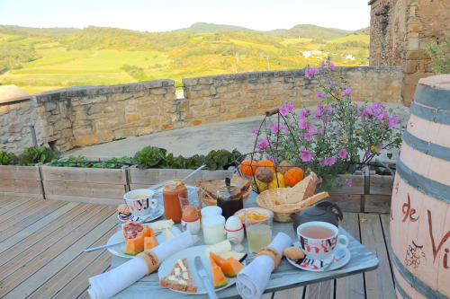 Breakfast table on castle terrace at Château de Villelongue with countryside views, pastries, fresh juice, and purple flowers