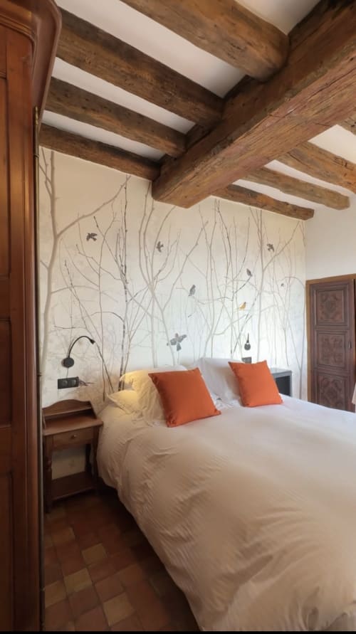 Chambre rustique aux poutres apparentes, literie blanche, oreillers orangés et fresque inspirée de la nature au B&B de Giverny.