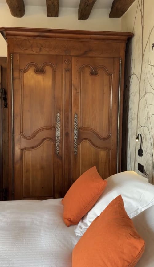 Chambre avec armoire en bois ouvragé, lit blanc aux coussins orange, poutres apparentes au Paradis de Lucile