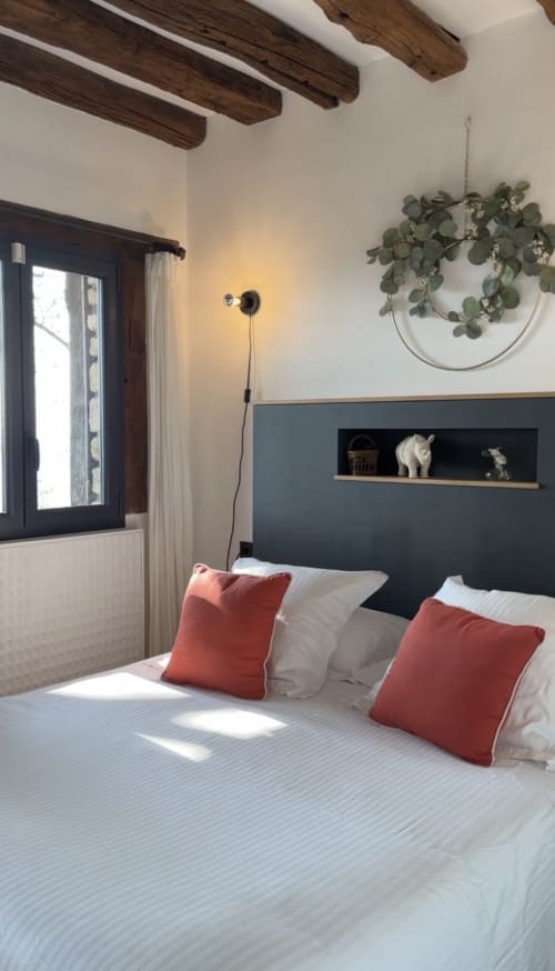 Chambre douillette avec tête de lit en ardoise, oreillers rouges, poutres en bois et eucalyptus suspendu au Paradis de Lucile