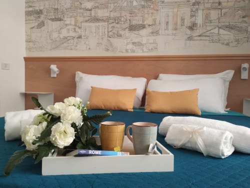 Camera da letto lussuosa a Campagnano di Roma con biancheria teal, fiori bianchi, tazze di benvenuto e arte murale architettonica.