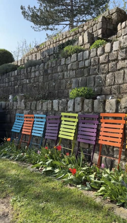 Chaises colorées empilées contre un mur de pierre ancien du cottage de La Roche Guyon près de Giverny, avec tulipes fleuries et verdure