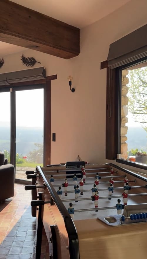 Table de baby-foot dans un séjour lumineux avec grandes fenêtres offrant vue panoramique sur la vallée fluviale près de Giverny