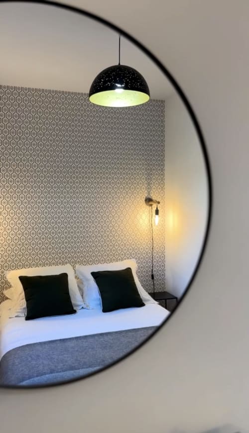 Chambre moderne avec luminaire suspendu noir, papier peint à motifs et literie blanche avec oreillers noirs chez Le Paradis de Lucile