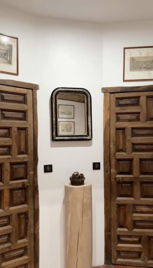 Intérieur rustique du Paradis de Lucile avec portes en bois, miroir encadré et sculpture sur piédestal, région de Giverny.
