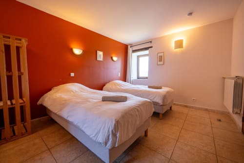 Three twin beds in Lou Cerisier room at Eco-hameau Lou Rey hostel, Le Collet de Dèze, with red accent wall and mountain views