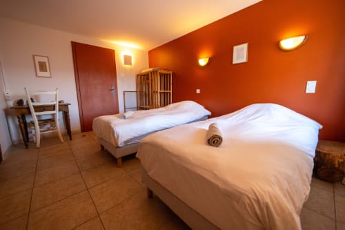 Spacious twin bedroom with burnt orange walls at Eco-hameau Lou Rey hostel in Le Collet de Dèze, France