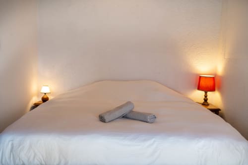 Cozy bedroom at Eco-hameau Lou Rey hostel with white bed, rolled towels, and warm bedside lamps