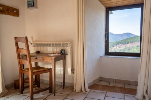 Mountain view room at Eco-hameau Lou Rey hostel with wooden desk, chair, radiator, and window overlooking Le Collet de Dèze