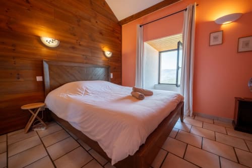 Cozy wooden bedroom at Eco-hameau Lou Rey with queen bed, orange walls, and mountain views from terrace