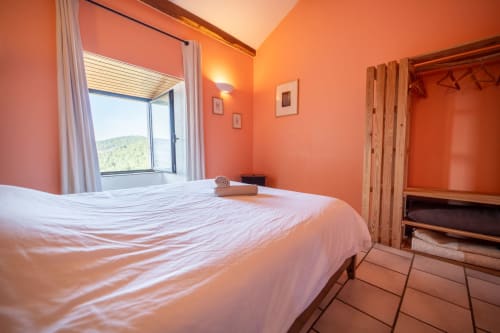 Bright orange bedroom with white bedding, mountain view window, and wooden wardrobe at Eco-hameau Lou Rey, Le Collet de Dèze