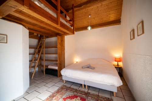 Cozy hostel bedroom at Eco-hameau Lou Rey with loft bed, queen bed, wooden beams, and warm lighting in Le Collet de Dèze.