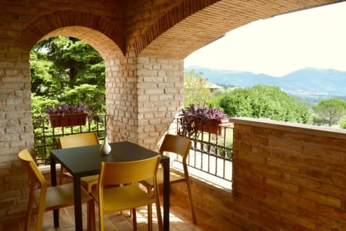 Tuscan terrace with dining table and yellow chairs overlooking green hills at Agriturismo Colle Mura, Gualdo Tadino