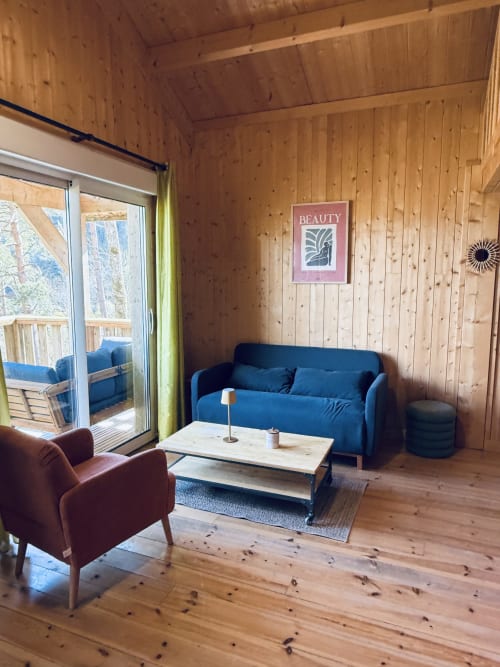 Accogliente living del lodge con divano blu, poltrona bordeaux, pareti in legno e vista lago presso Cabanes et lodges du Belvédère