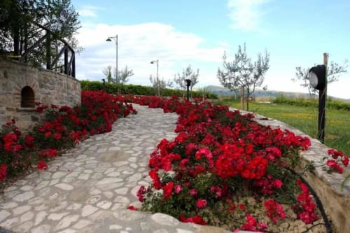Red flowering garden pathway at Agriturismo Colle Mura in Gualdo Tadino, Italy with stone structures and countryside views