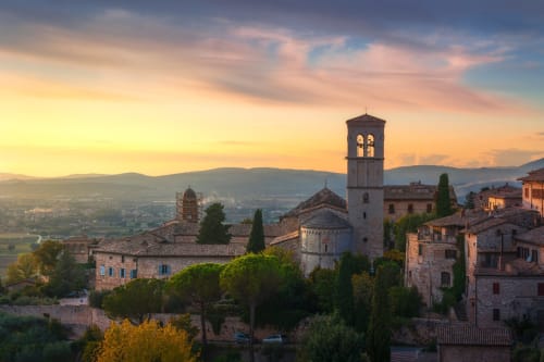 Medieval Umbrian town at sunset with bell tower, stone buildings, cypress trees, and valley view near Gualdo Tadino